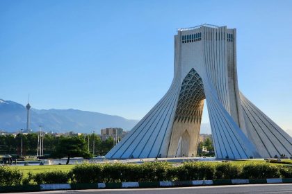 Capture of the iconic Azadi Tower in Tehran with a mountainous backdrop and clear sky.