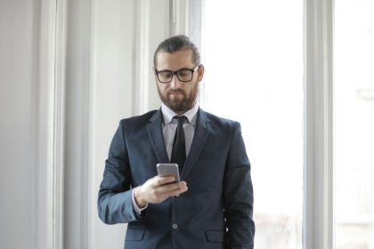 Confident man in formal suit using smartphone by window in office setting.