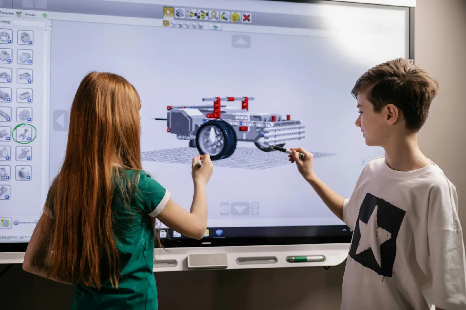 A boy and girl collaborate on a robotics project using a digital screen in a classroom setting.