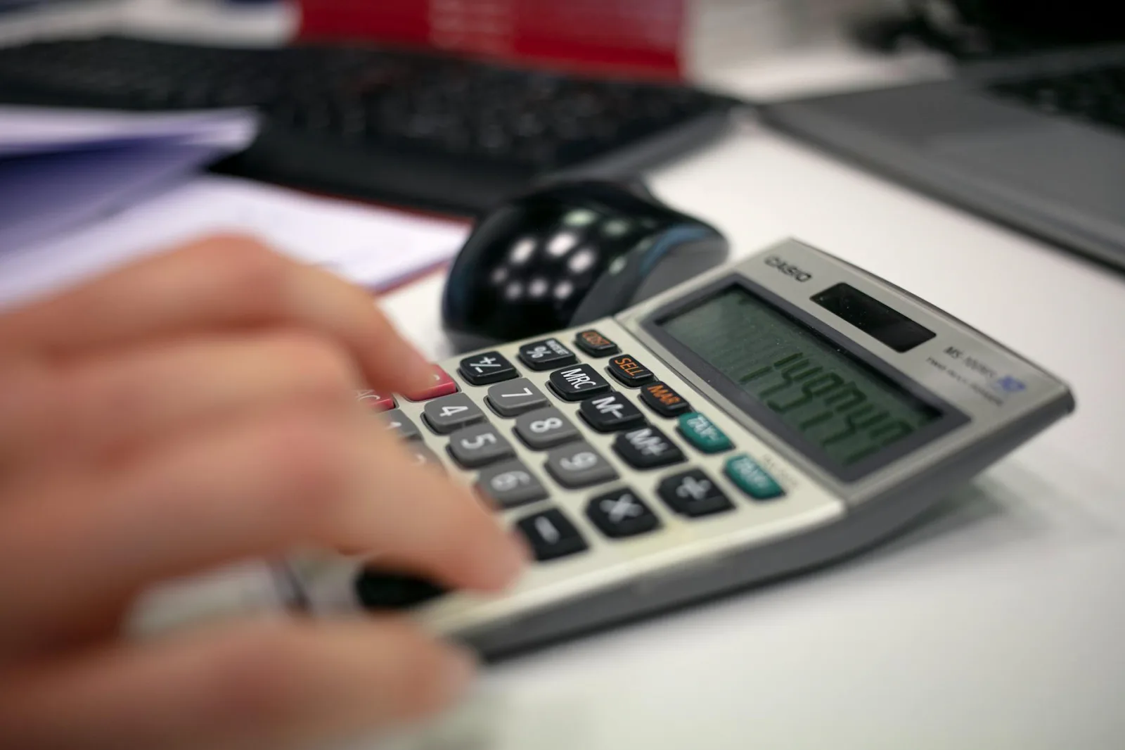 Close-up of a hand using a calculator on an office desk for accurate calculations.