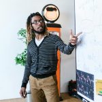 Man explaining cryptocurrency concepts on a whiteboard in a modern office setting.