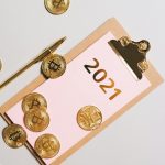 Top view of golden Bitcoin coins scattered on clipboard with 2021 text, symbolizing wealth.