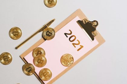 Top view of golden Bitcoin coins scattered on clipboard with 2021 text, symbolizing wealth.