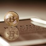Close-up of a gold Bitcoin reflecting on a digital tablet screen, showcasing cryptocurrency concepts.