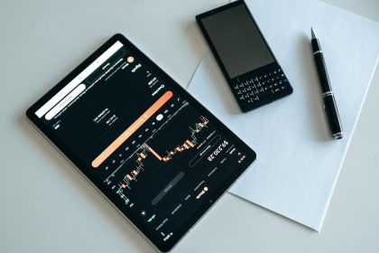 Top view of a workspace with a tablet displaying financial charts, a smartphone, pen, and paper.